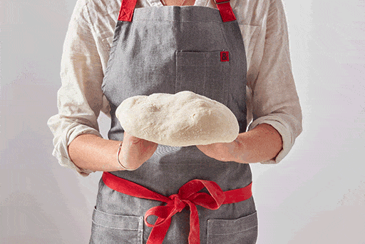 A baker holding a piece of dough over their knuckles, slowly turning the dough to stretch it into a round shape. 