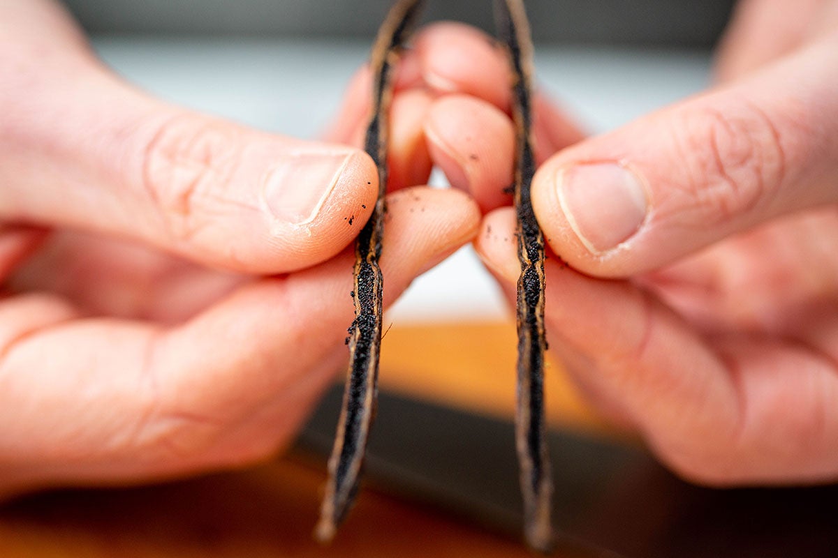 A baker's hands holding a Madagascar vanilla bean that's been split lengthwise to reveal the vanilla seeds inside.