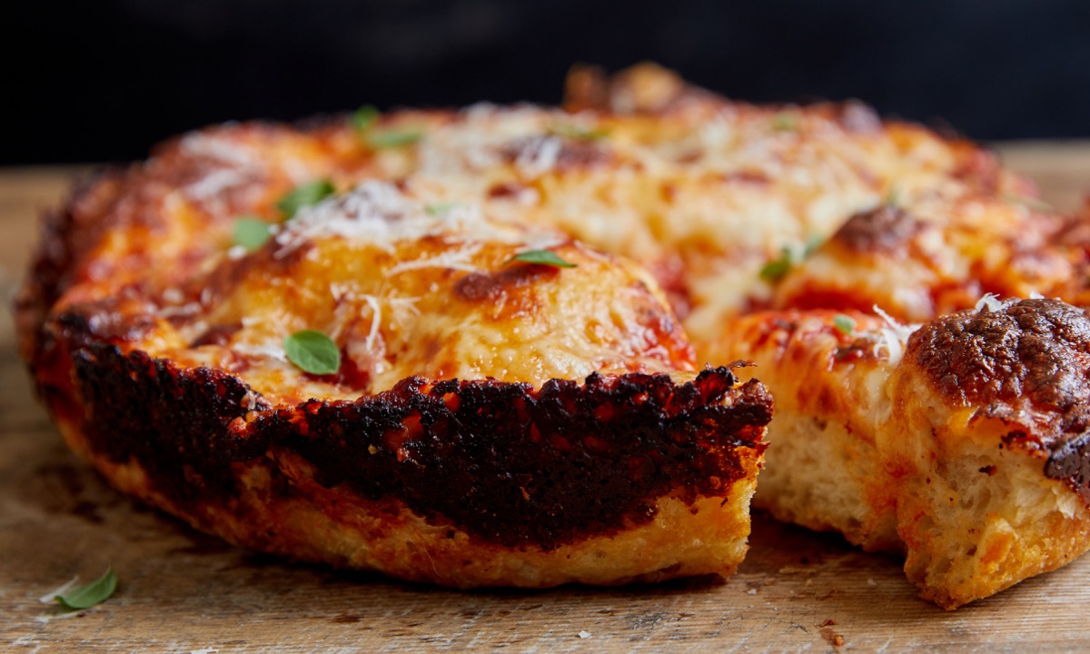 Baked thick-crust pizza showing its heavily charred cheesy edge.