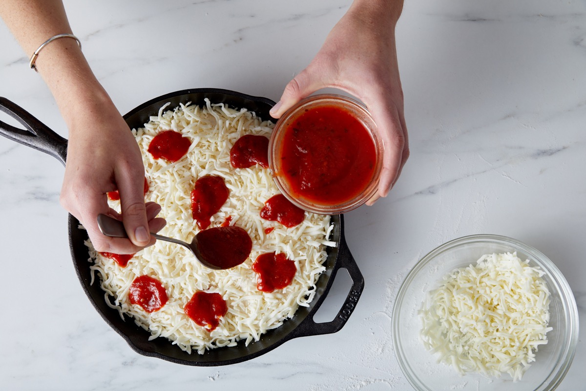 Tomato sauce being dolloped atop a cheese-topped pizza before baking.
