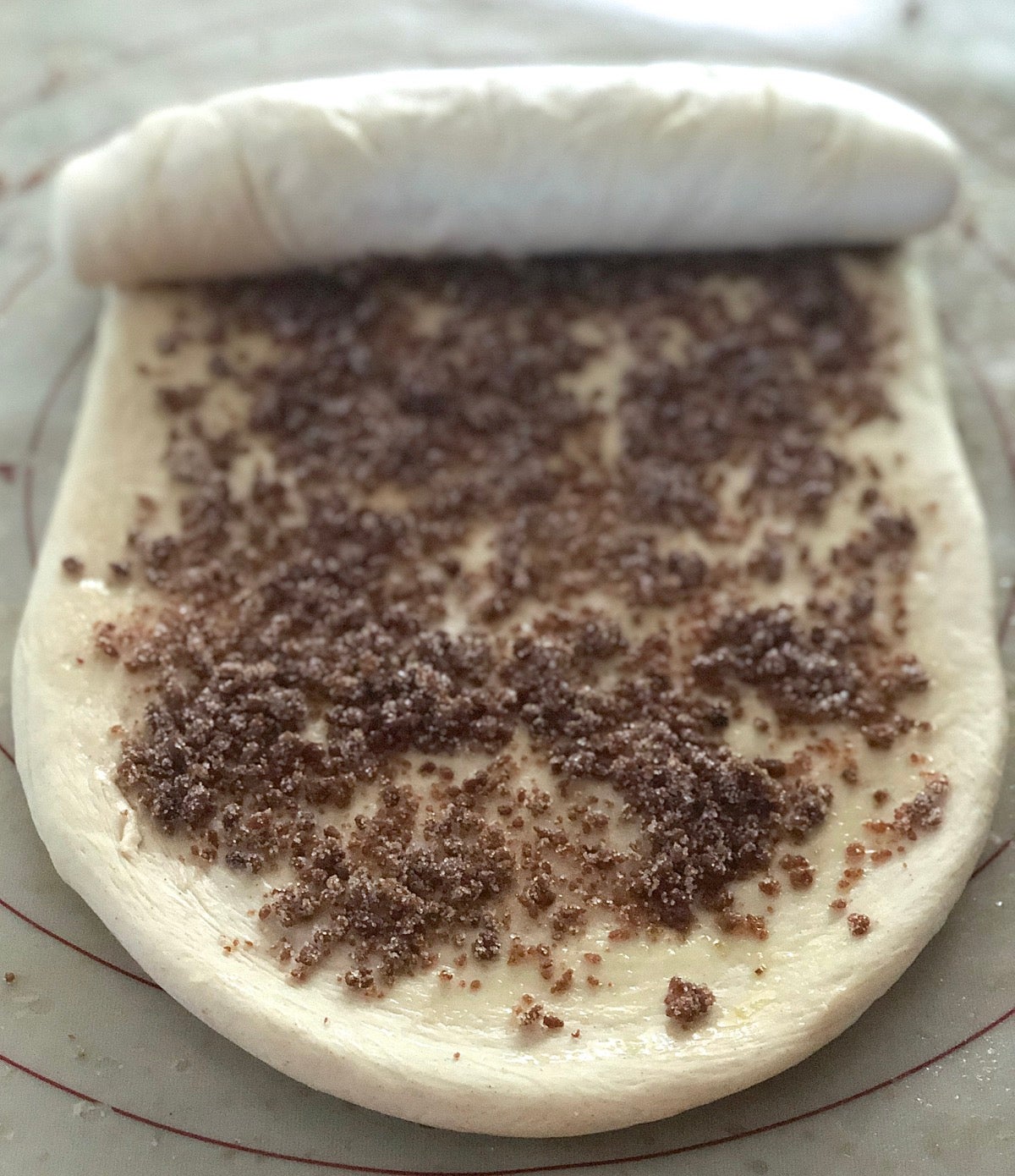 The dough for a cinnamon swirl loaf, sprinkled with filling and being rolled into a log.