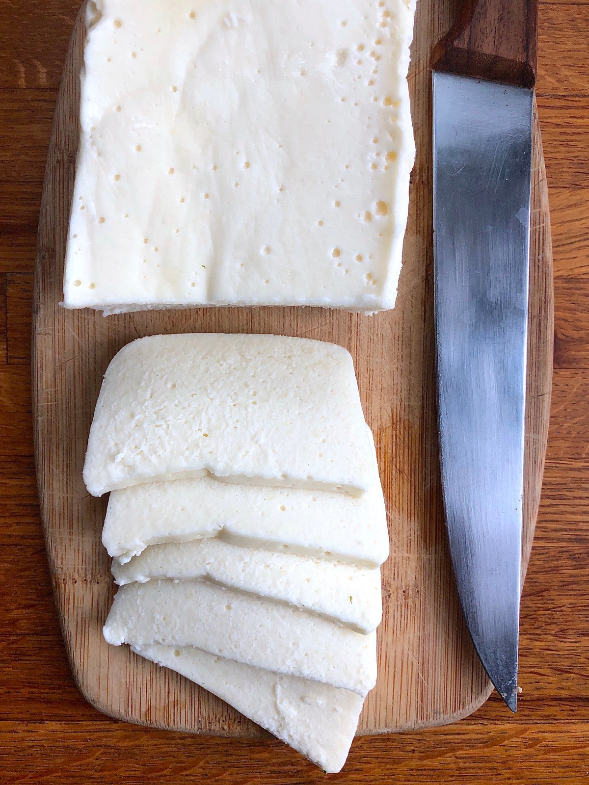 Chunk of blended cheeses — Asiago, Parmesan, and cheddar — sliced on a cutting board.