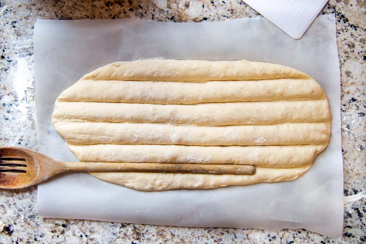 Shaped bread dough with wooden spoon making grooves