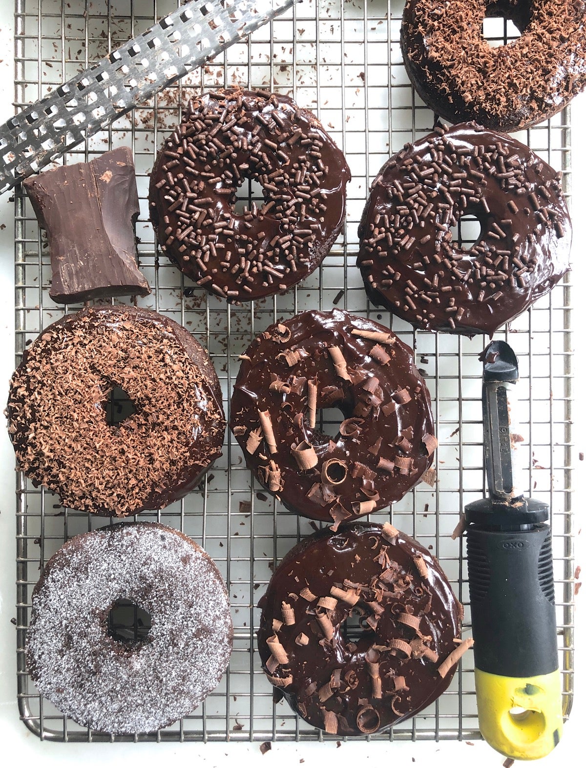 Frosted and sprinkled Chocolate Fudge Cake Doughnuts on a cooling rack.