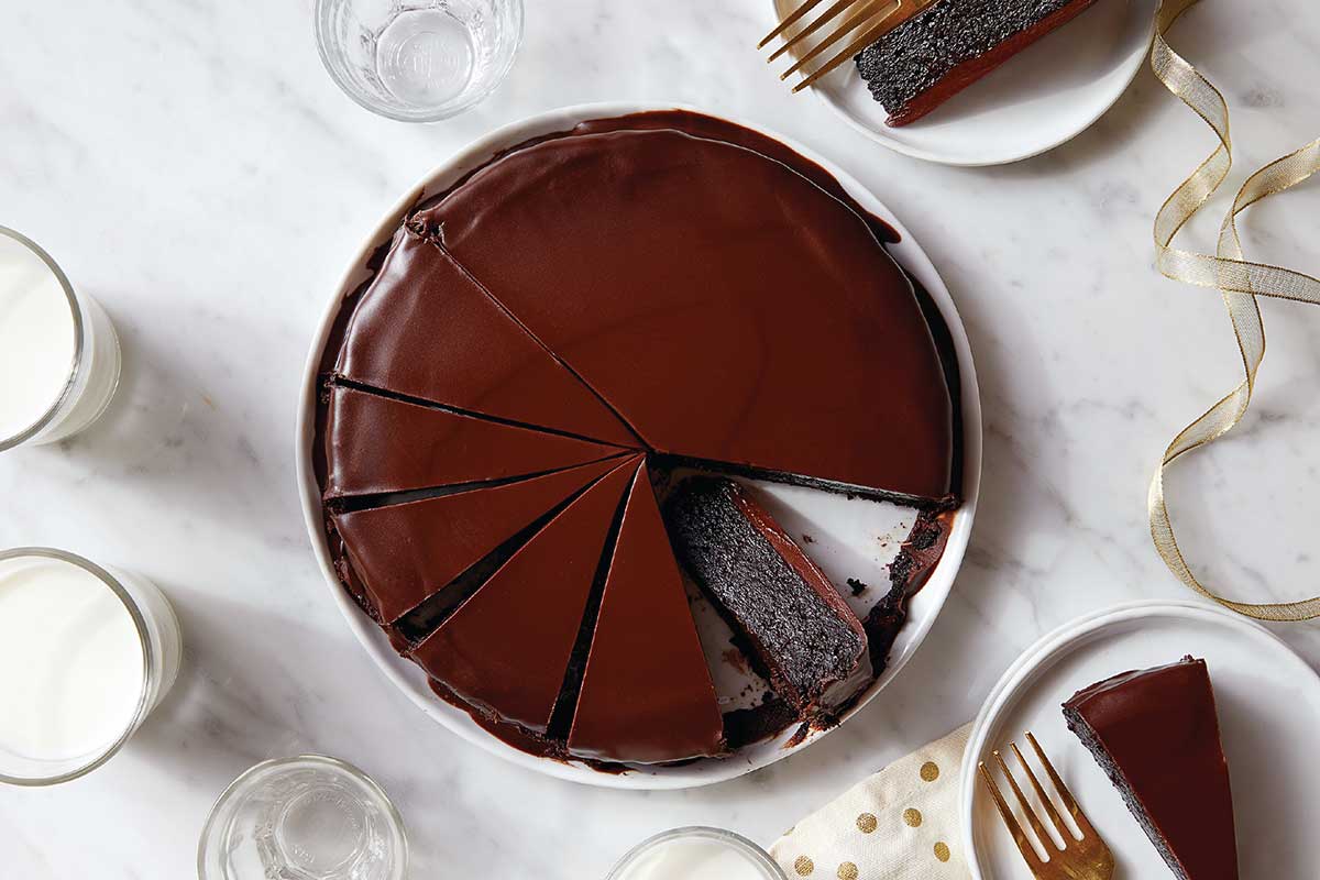 A flourless chocolate cake topped with ganache on a serving plate, cut into slices