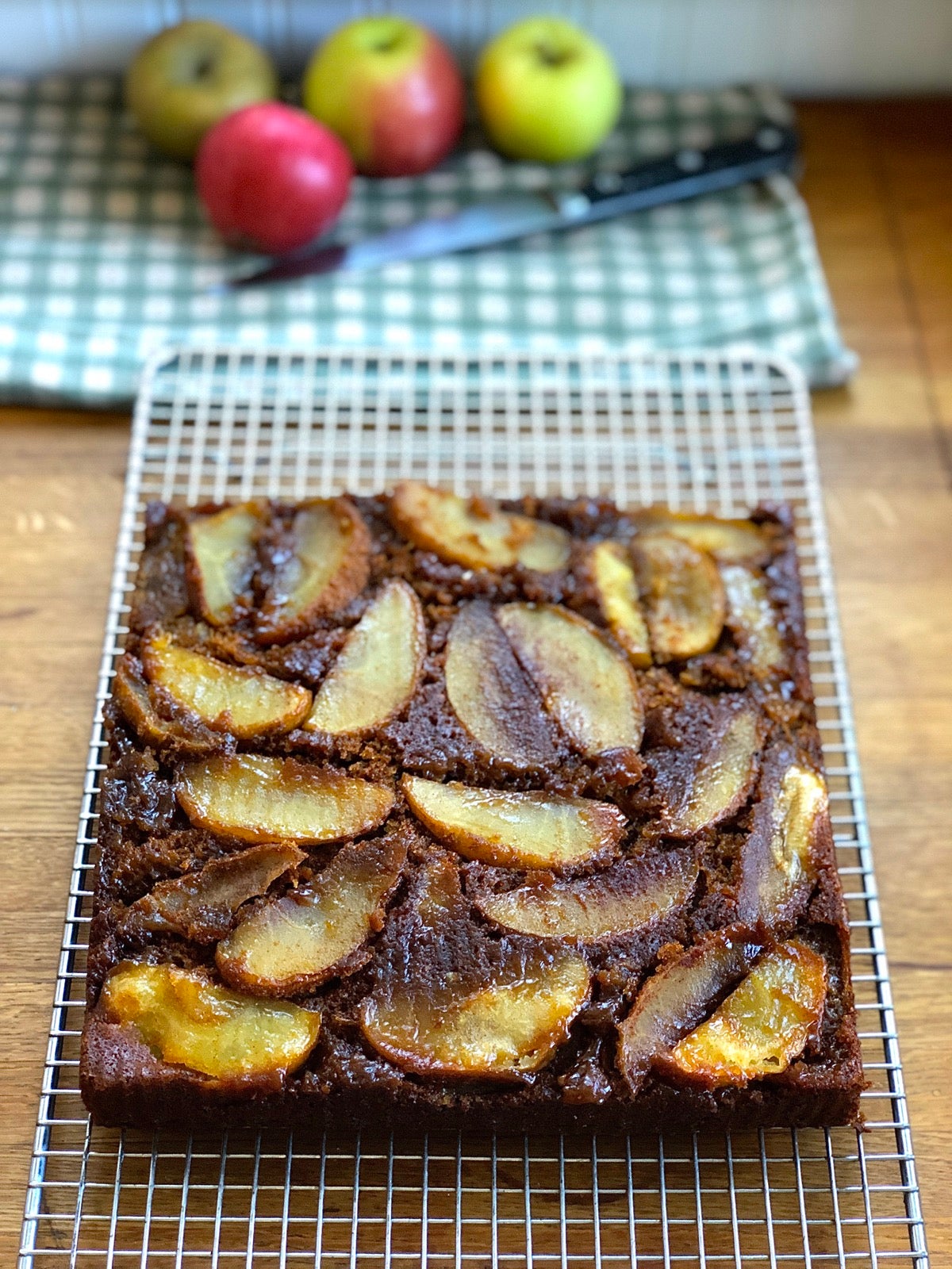 Apple upside-down gingerbread cake cooling in a pan on a rack.