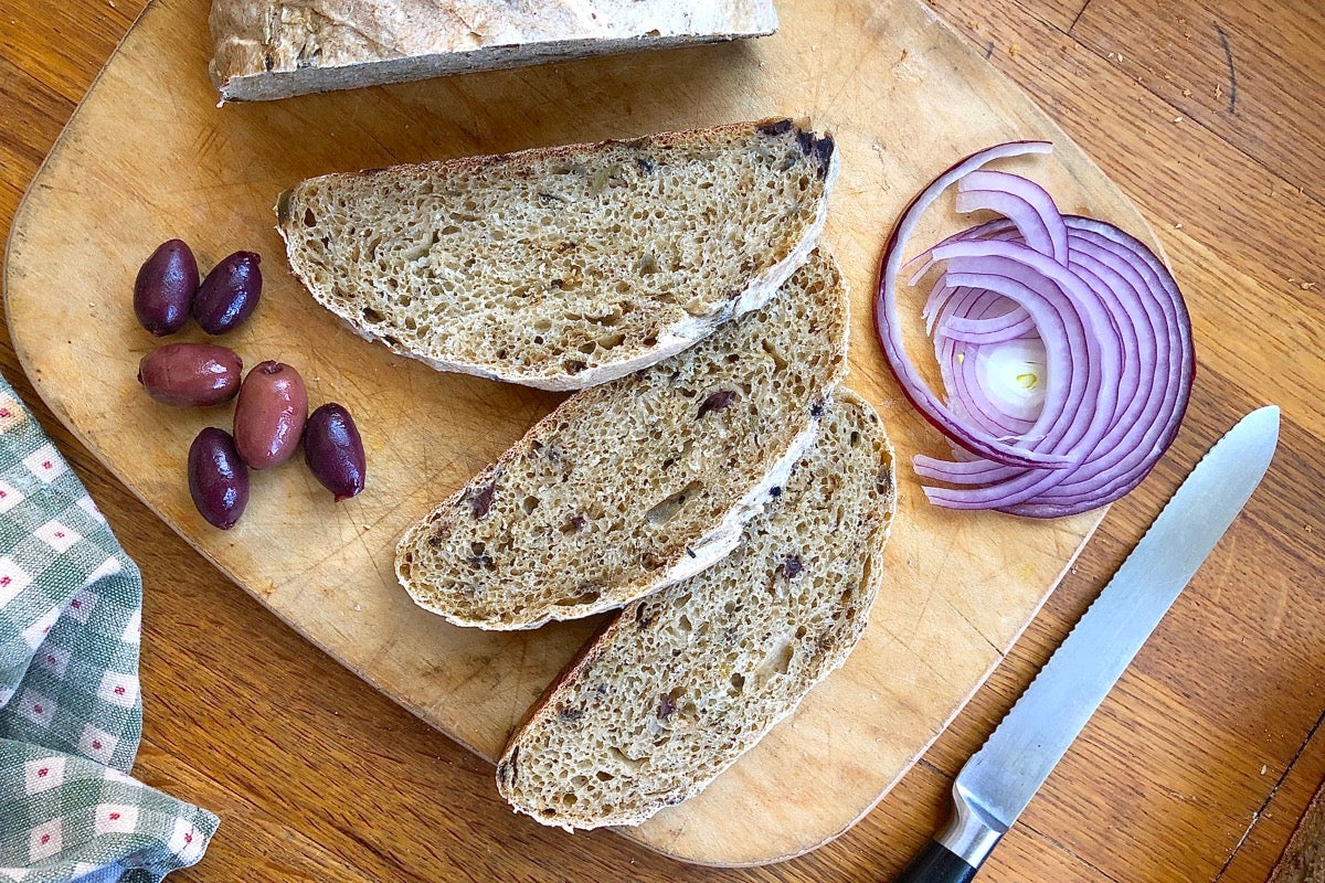 Greek Olive and Onion Bread sliced on a cutting board, with kalamata olives and red onion