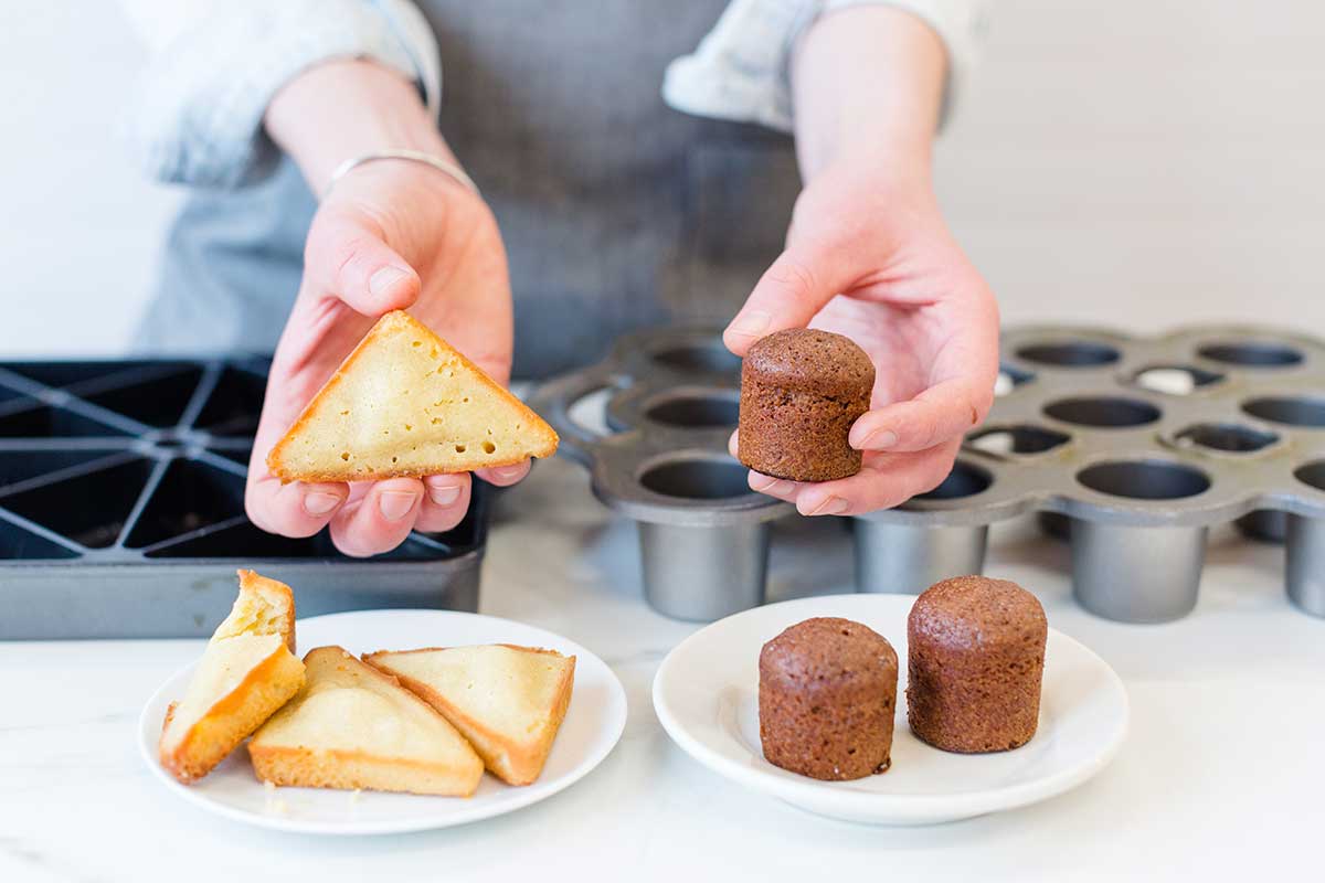 A baker holding up madeleines baked a in mini scone pan and a mini popover pan