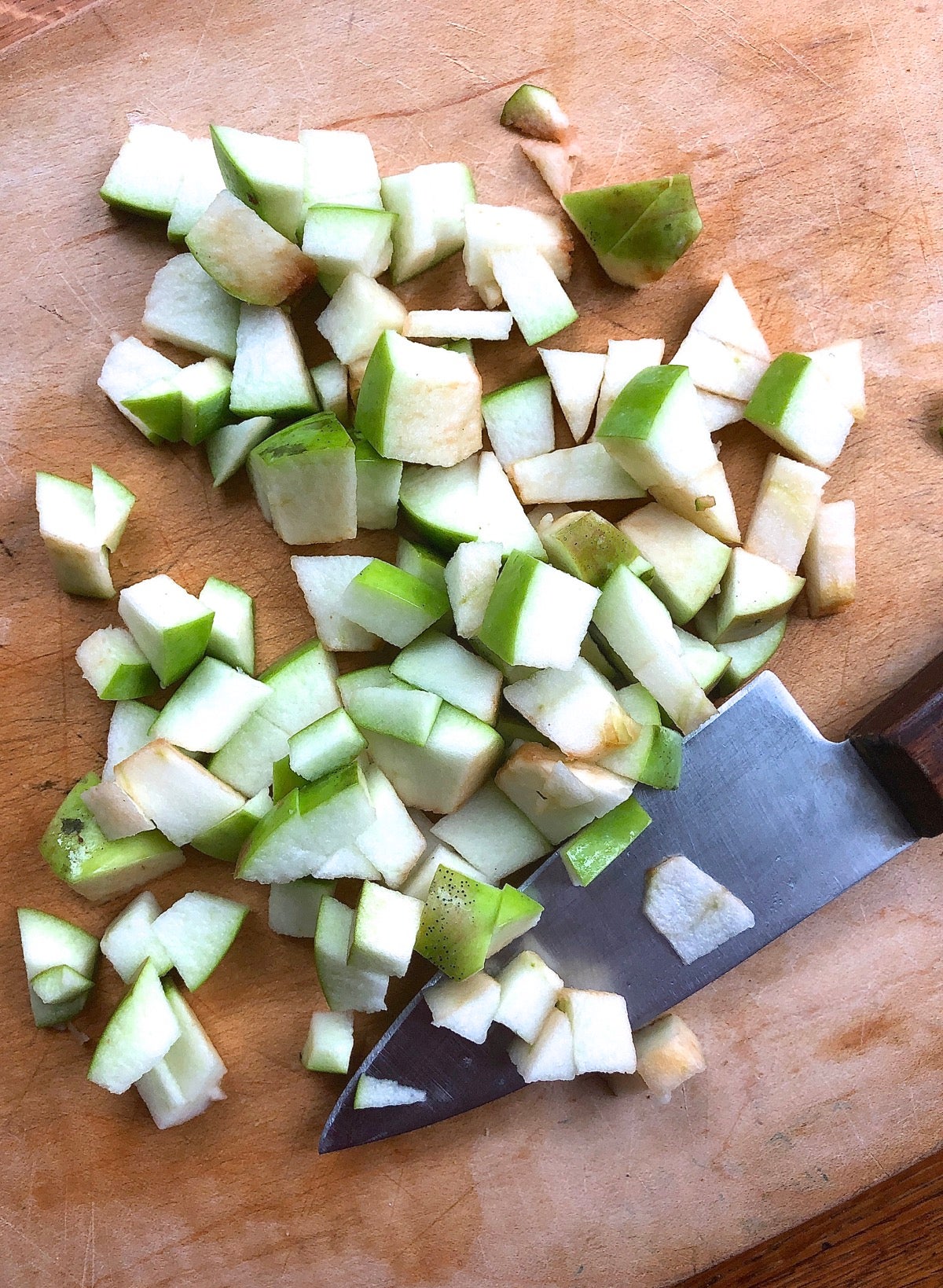 Unpeeled green apples chopped on a cutting board with a chef's knife.