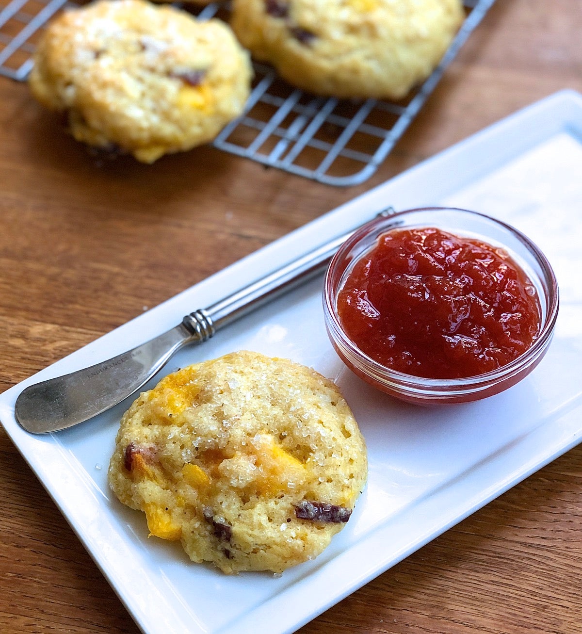 A peach scone on a plate with a butter knife and bowl of peach preserves, ready to enjoy.