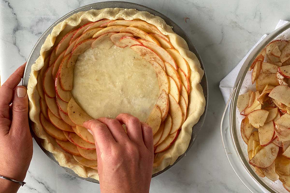 A baker assembling a rose apple pie by layering thinly sliced apples on top of one another in concentric rings