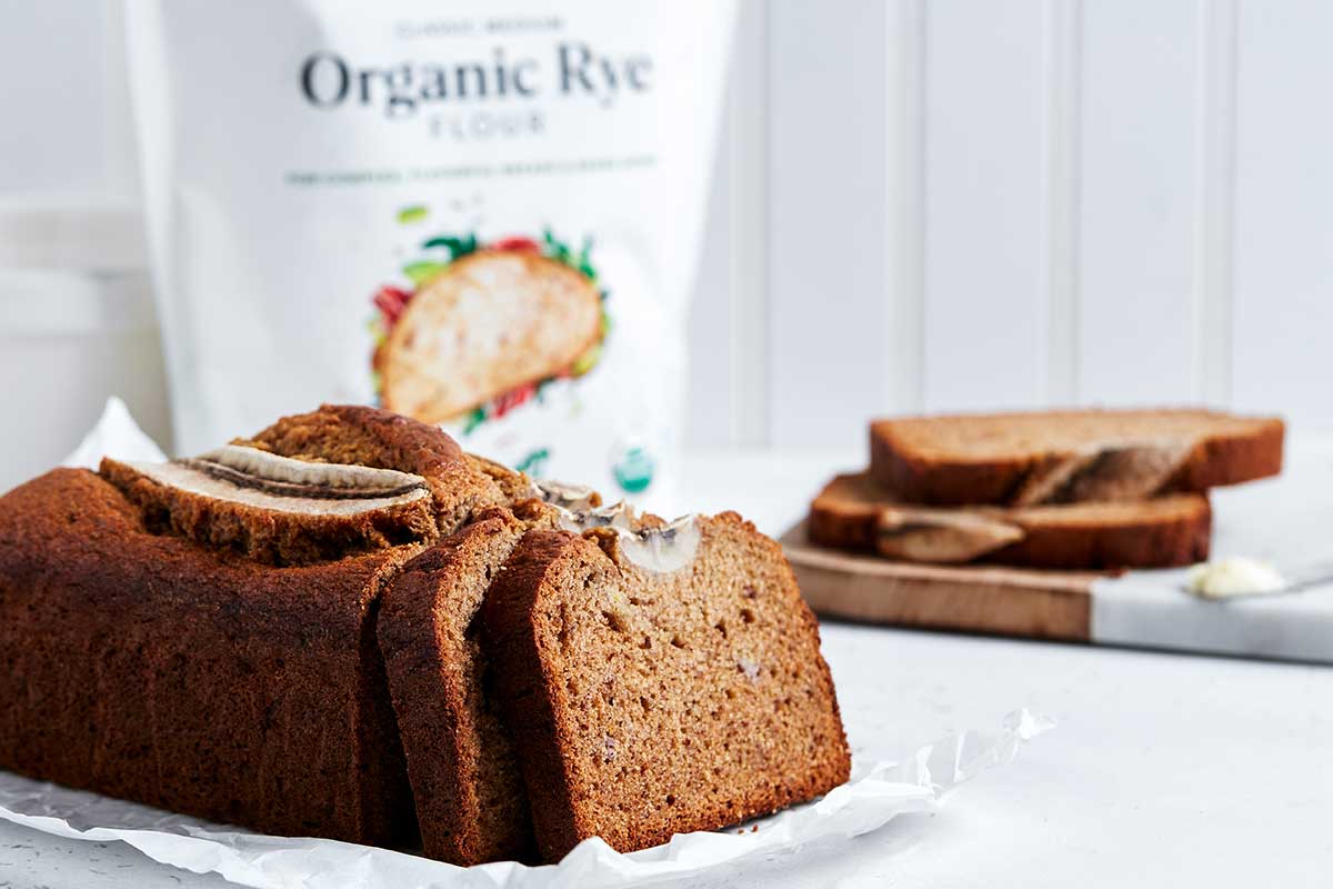 A loaf of rye banana bread next to a bag of King Arthur Organic Medium Rye Flour