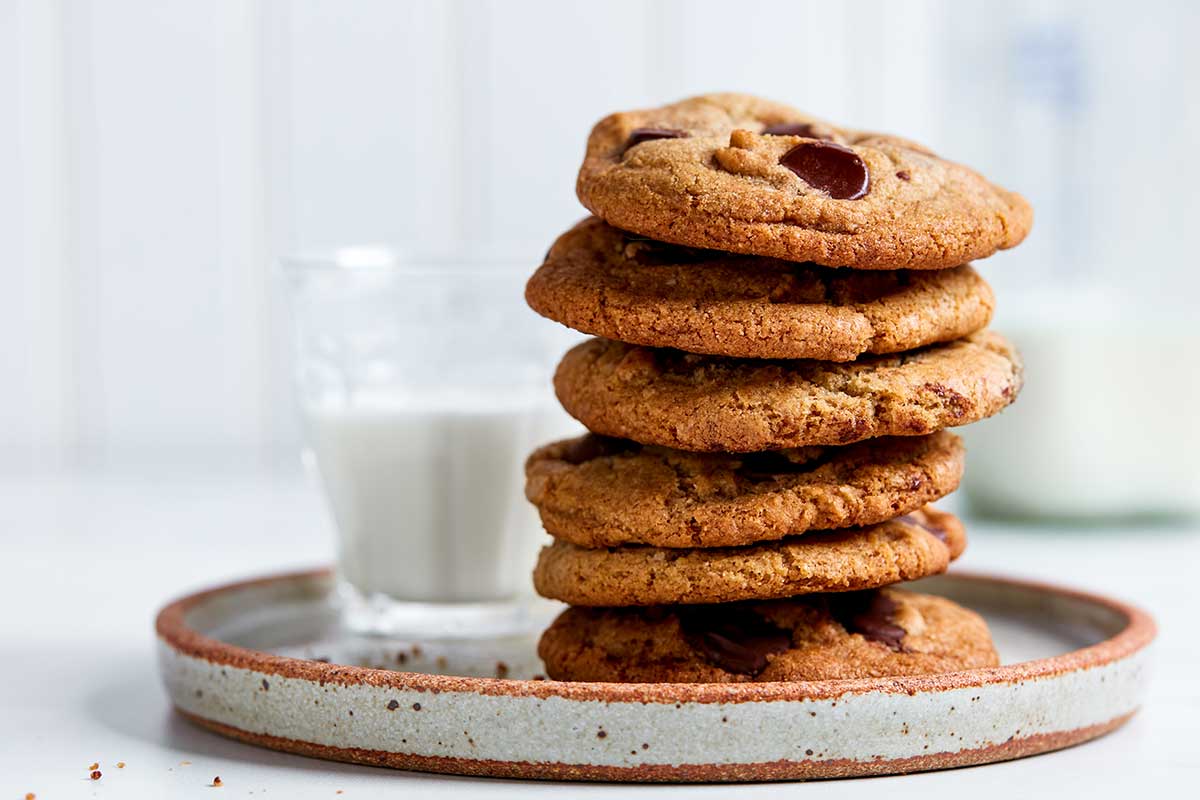 A stack of rye chocolate chip cookies on a plate next to a glass of milk