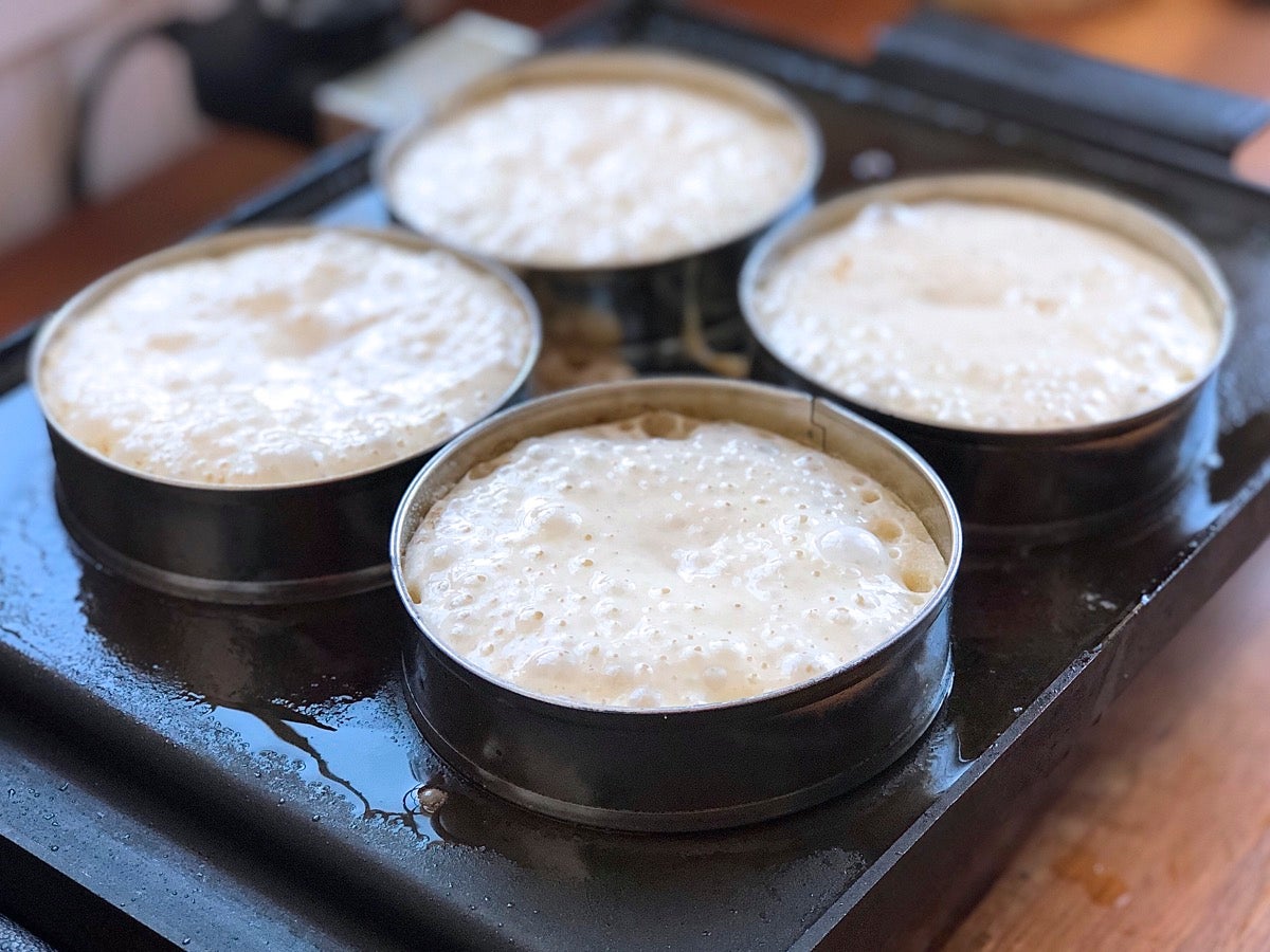 Four sourdough crumpets cooking on a griddle.