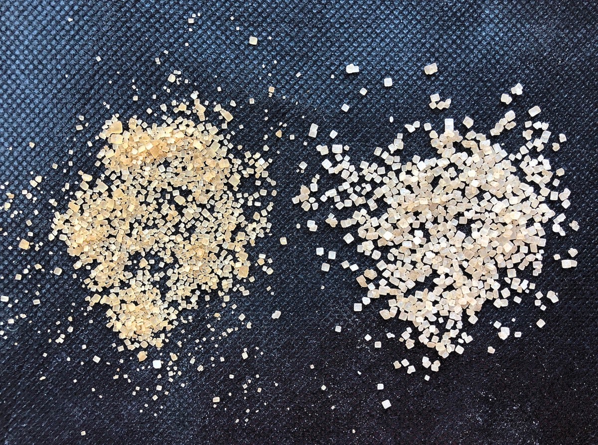 Two types of turbinado sugar sprinkled on a dark background to show two different grain sizes.