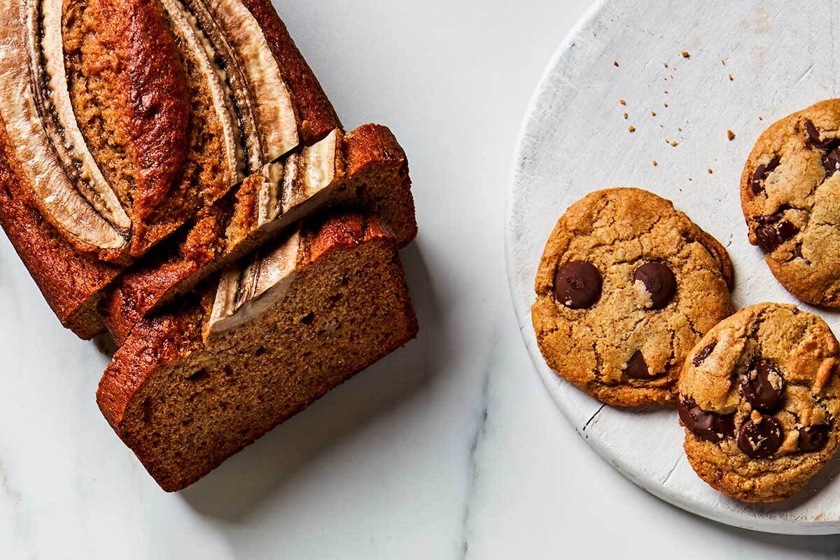 A loaf of rye banana bread cut into slices next to rye chocolate chip cookies