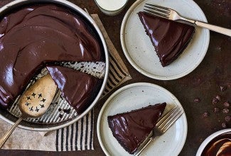 A chocolate cake pan cake topped with chocolate frosting and a few slices on plates