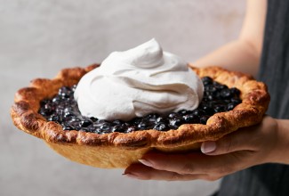 Baker holding whole blueberry pie outside of its pan