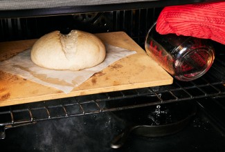 Baker pouring hot water into cast iron skillet to steam bread while baking
