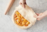 Baker putting top pie crust over filling in pie pan