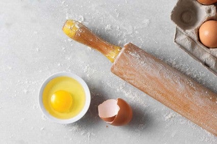 A cracked egg in a small bowl next to a rolling pin