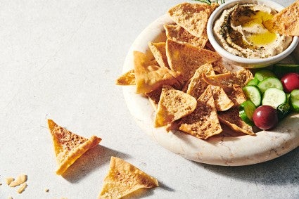 A bowl of homemade pita chips with dip in the center