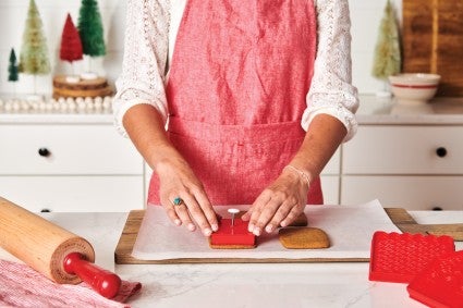 Baker using pop-out gingerbread house cutters to finalize design in baked cookies