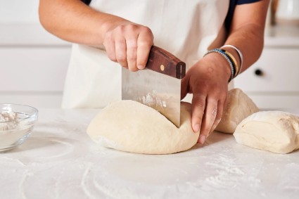Baker cutting bread dough in half with a bench knife