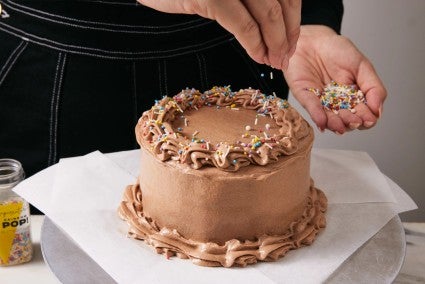 Chocolate cake being garnished with rainbow sprinkles