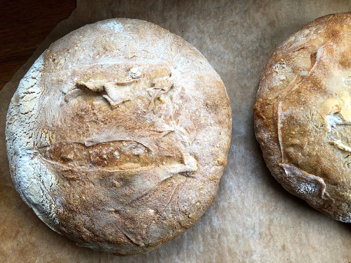 Two round loaves of bread, just out of the oven, on a piece of parchment.