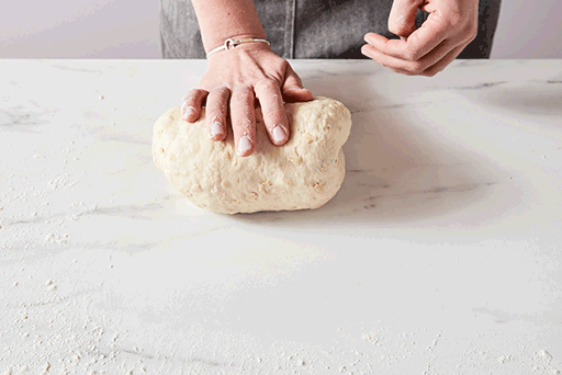 A baker kneading dough by hand on a countertop. 