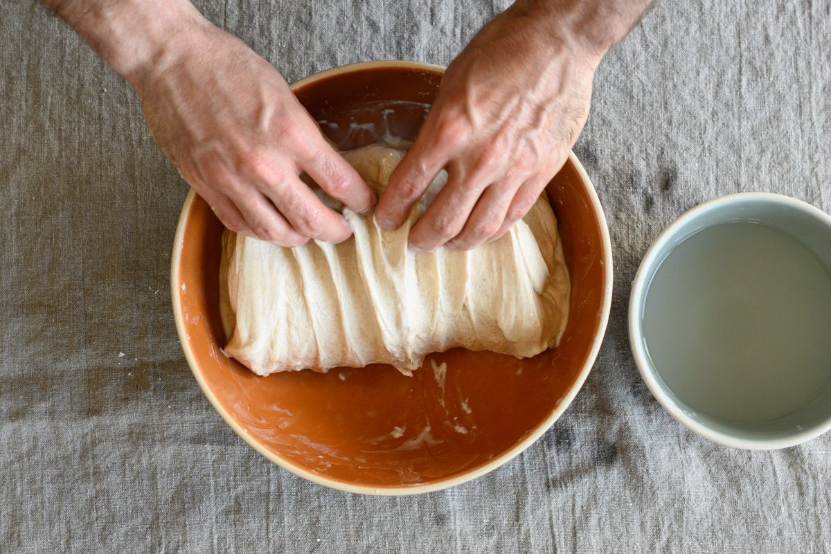 A baker folds bread dough in a bowl