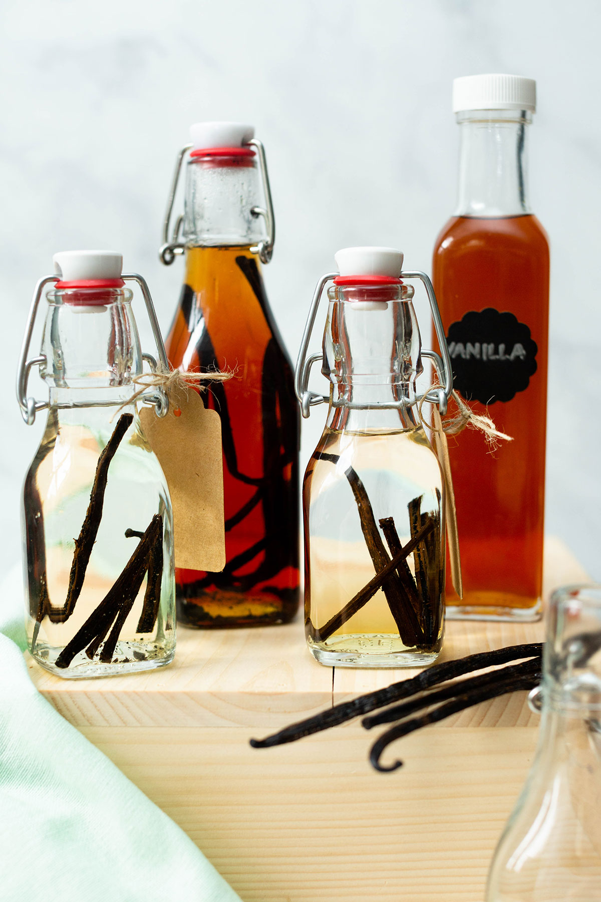 Small and large bottles of vanilla extract that have been aged for varying amounts of time, as well as a few vanilla beans.