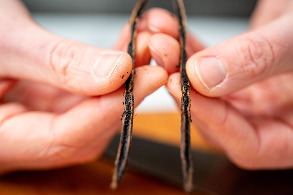 A baker's hands holding a Madagascar vanilla bean that's been split lengthwise to reveal the vanilla seeds inside.