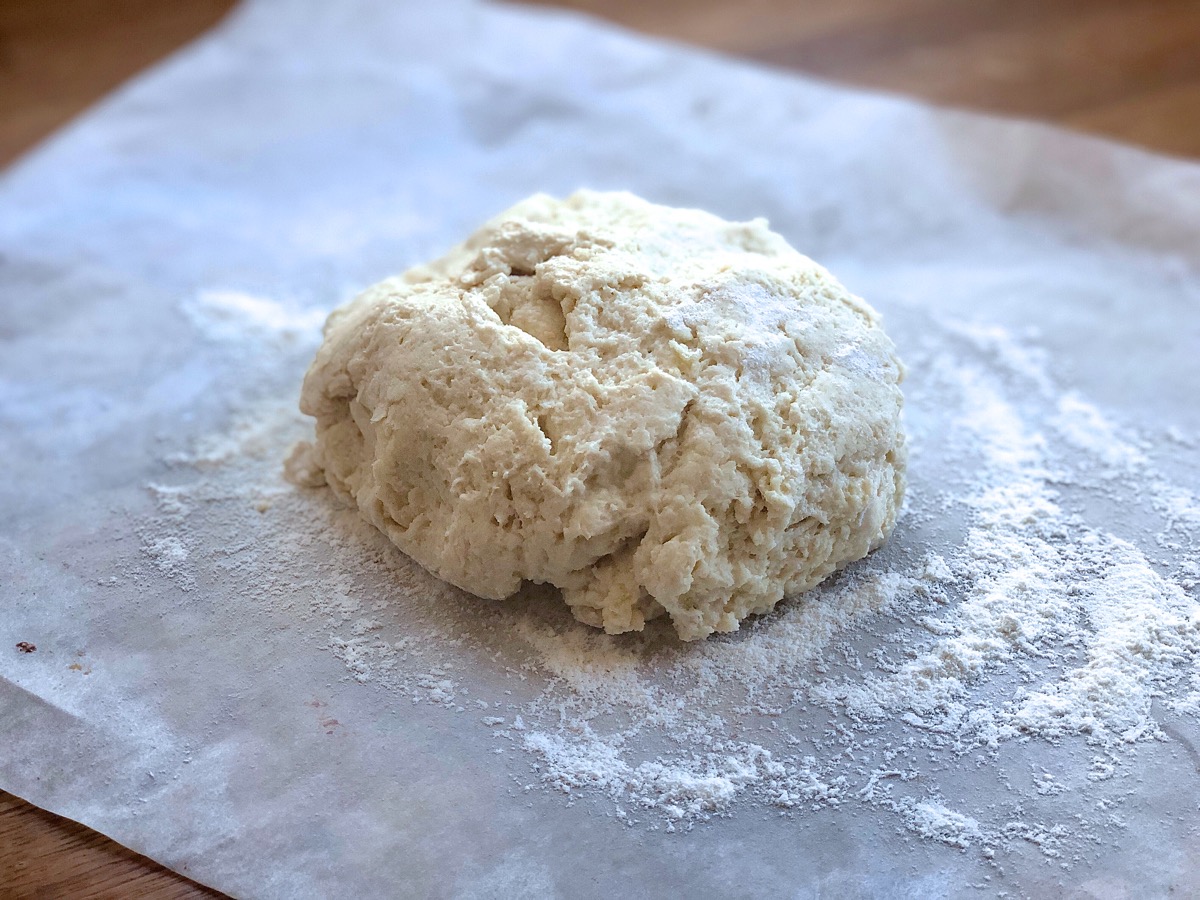 Biscuit dough on a floured piece of parchment waiting to be shaped.