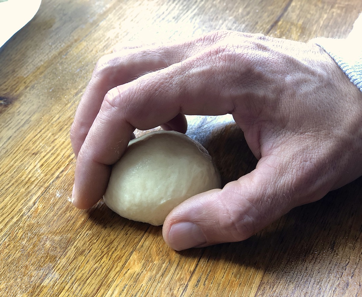 Hand cupped over ball of dough, showing the position for rolling it into a smooth ball.
