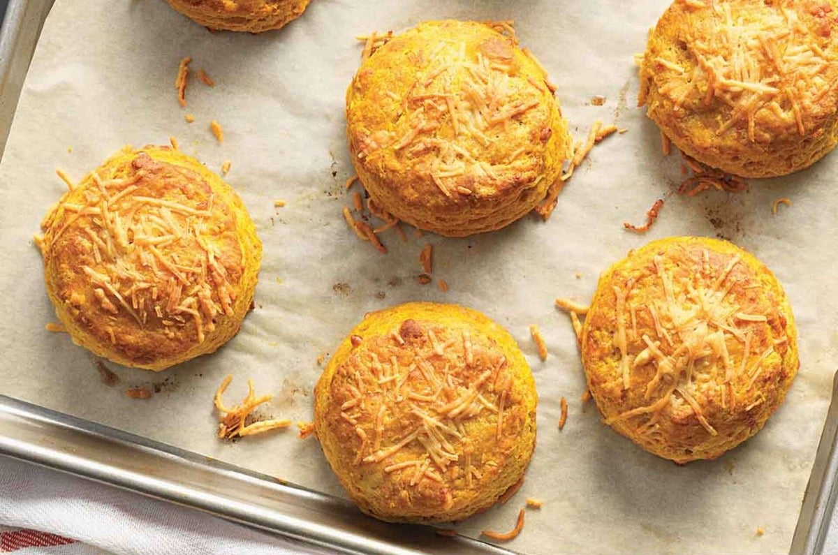 Bright gold pumpkin cheddar biscuits on a baking sheet.