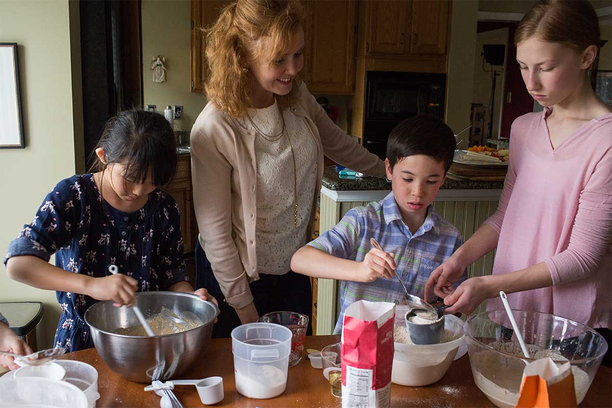 A mother surrounded by three children all baking together in the kitchen