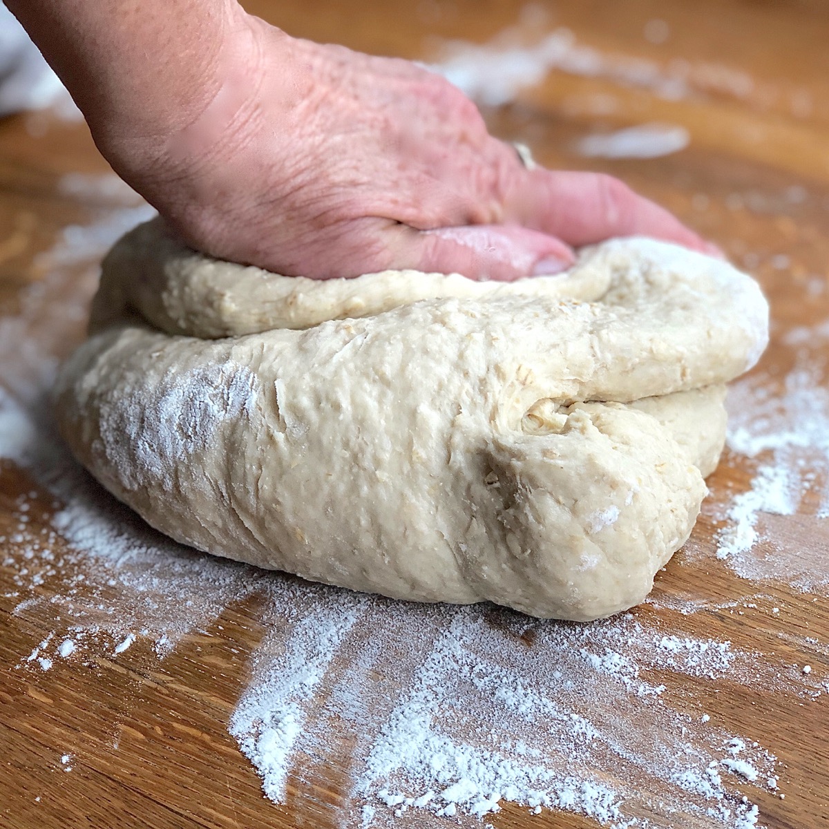 Hand-kneading oatmeal bread dough on a floured board
