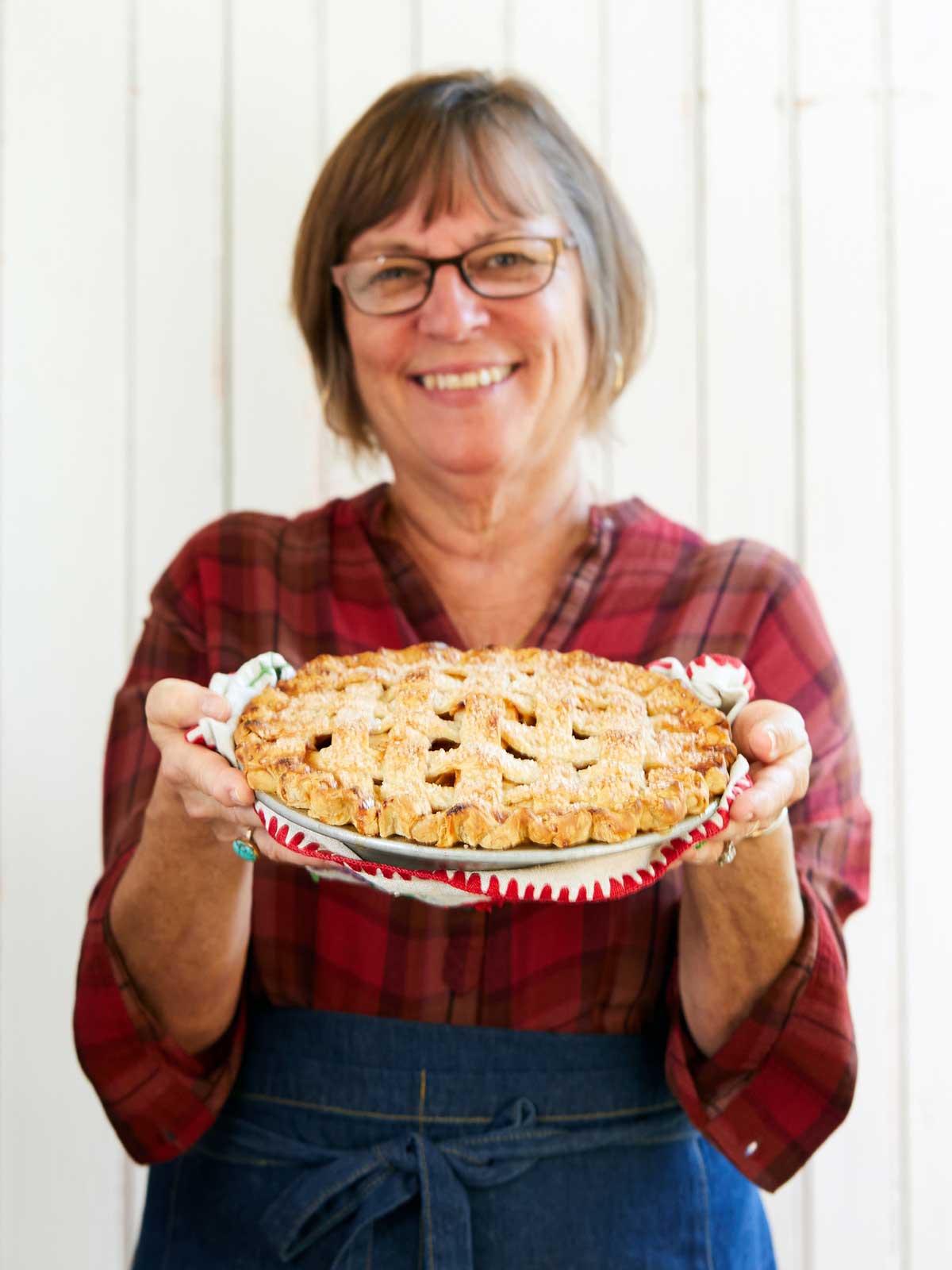 A woman holding out a lattice-topped apple pie, smiling