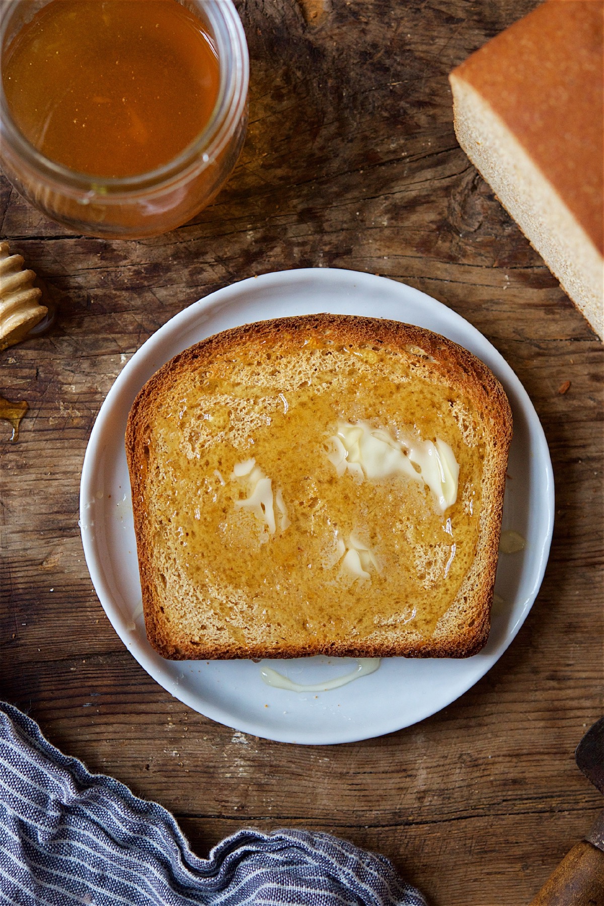 A slice of Classic 100% Whole Wheat Bread on a plate, lightly toasted and topped with melting butter and honey.
