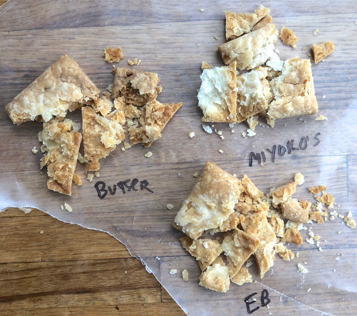 Three small squares of pie pastry made with three types of butter, crushed slightly to show their flaky texture