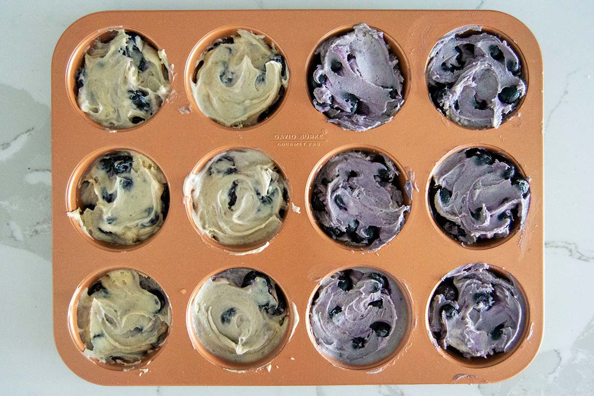 Muffin tin with golden blueberry muffin batter on left, blueish batter on right