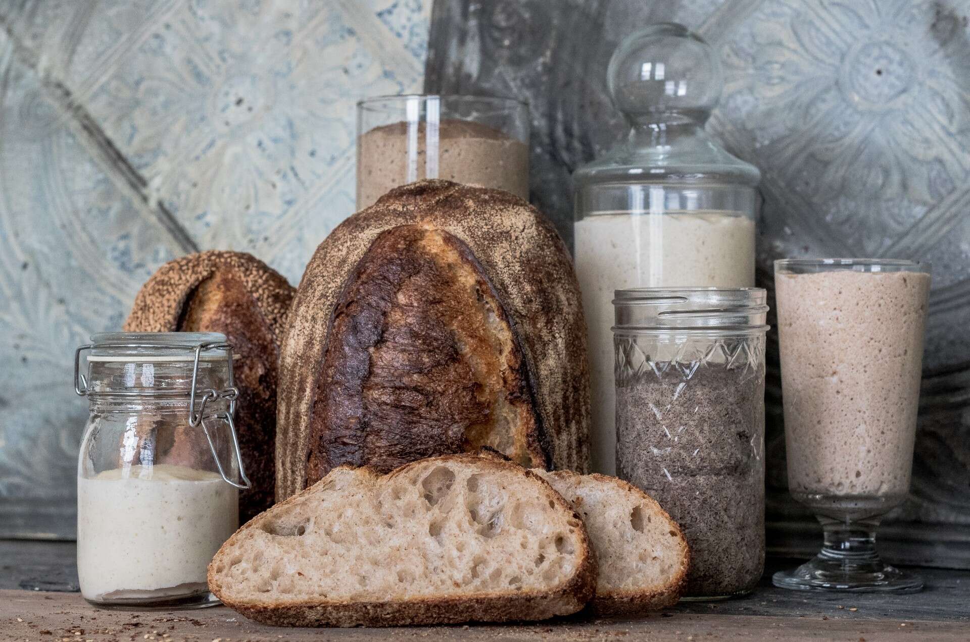 A series of preferments in jars on a table with bread