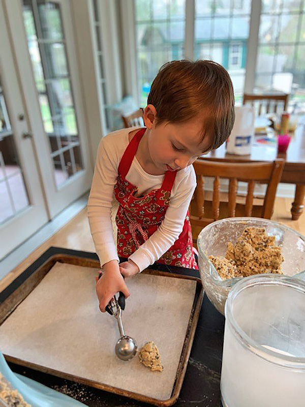 A young baker using a cookie scoop to scoop dough onto a baking sheet
