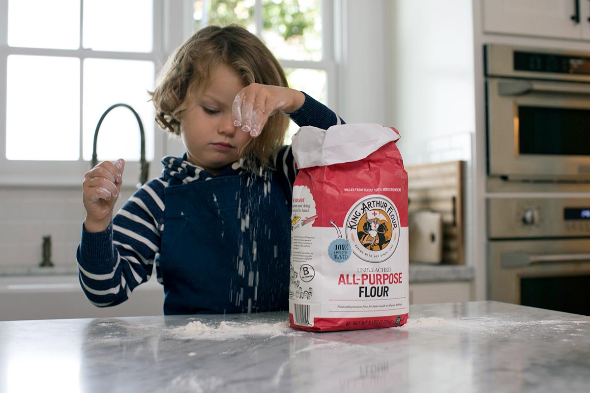A child playing with King Arthur Flour on a kitchen counter