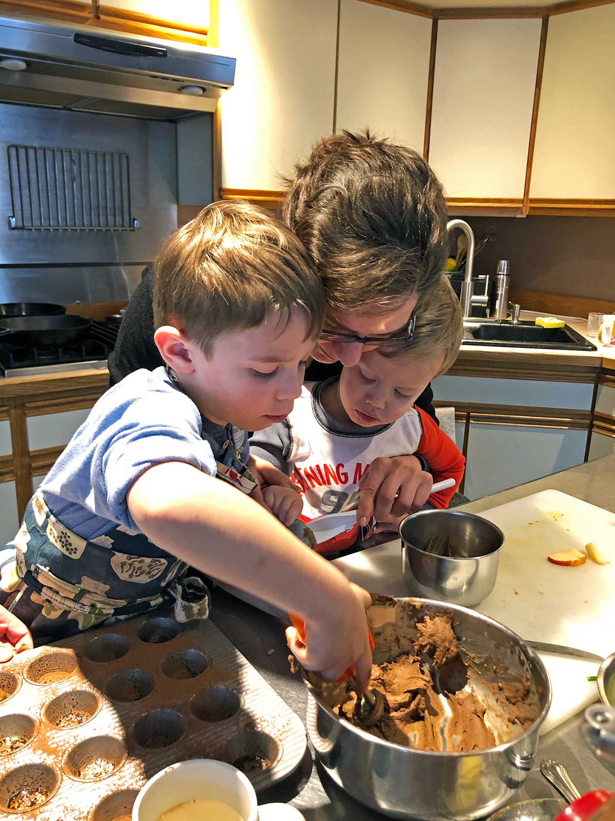 A mother and her two children scooping batter out of a bowl into a mini muffin pan.