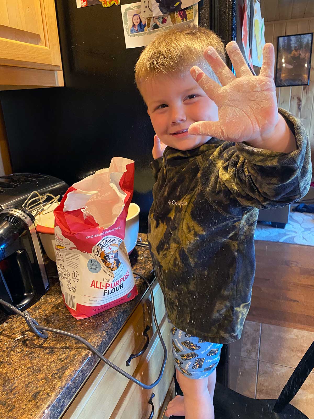 A child with a bag of King Arthur Flour in the kitchen holding out a flour-covered hand