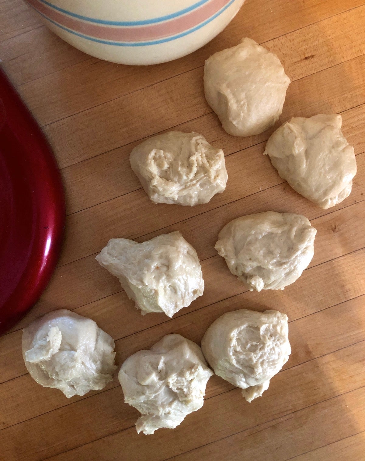 Eight rough pieces of dough sitting on a wooden table, waiting to be shaped into perfect round balls.