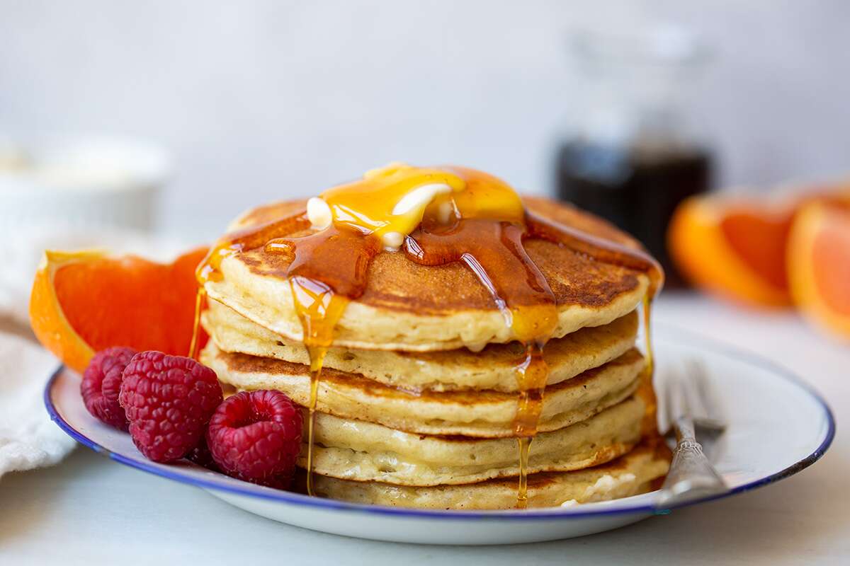 A stack of pancakes topped with butter, fruit, and maple syrup